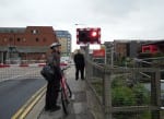 a photo of a man with a bike stood beside the Brayford Wharf East train barriers.