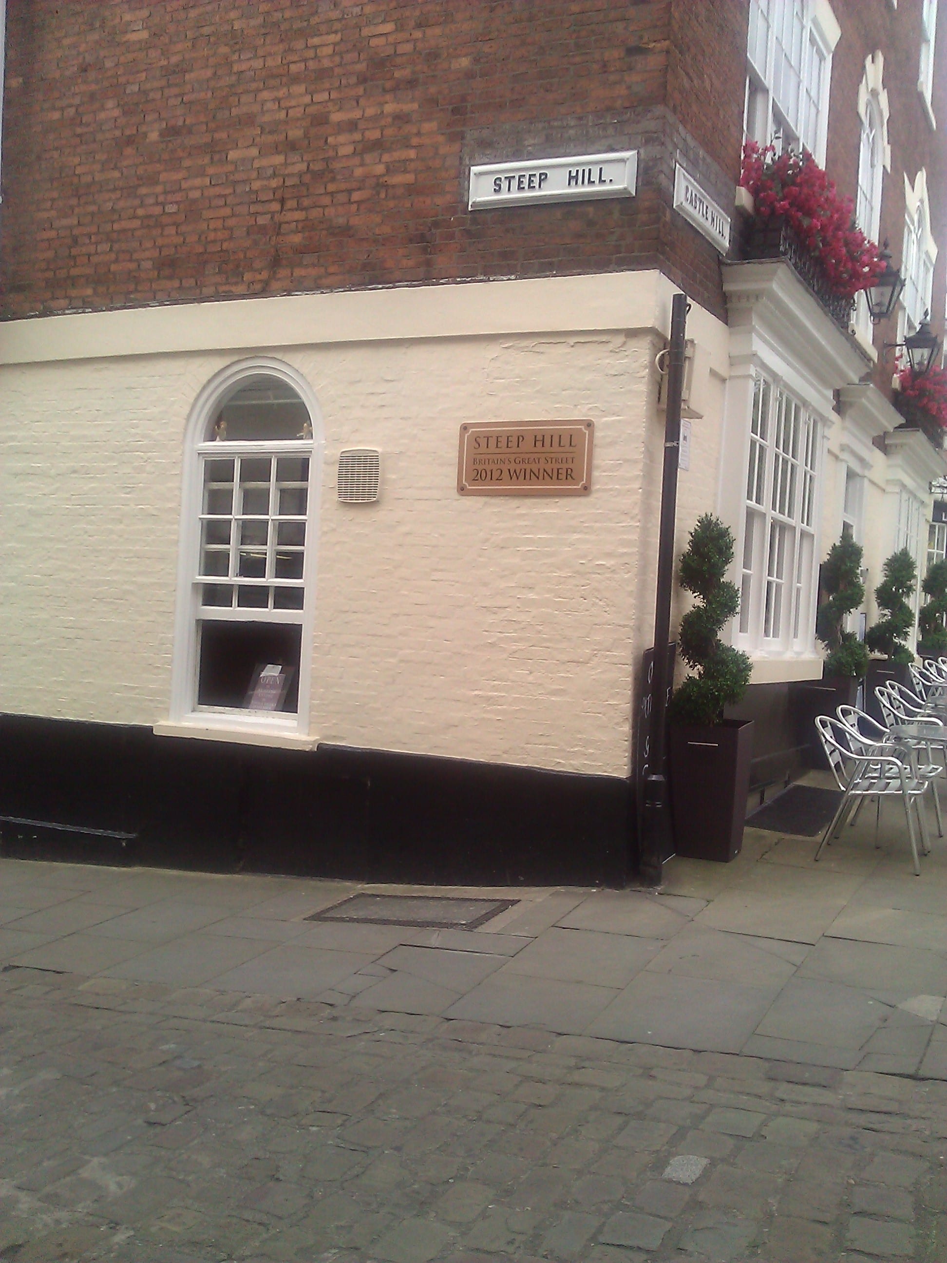 A street sign for Steep Hill, on the side of a cafe at the top. Also displays the Best Street award.