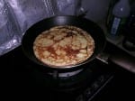 A pancake cooking in a frying pan.